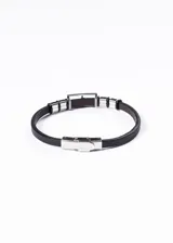 Pulsera de cuero negro con apliques de acero inoxidable plateado. En el centro presenta un dije rectangular con un águila grabada.