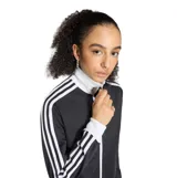 Campera deportiva Adidas Classic TT de color negro con cierre frontal blanco, cuello alto y las icónicas tres tiras blancas en las mangas. Cuenta con el logotipo del trébol bordado en el pecho.