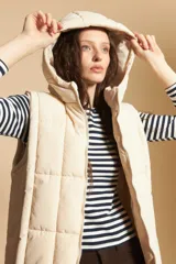Chaleco acolchado de nylon color beige, con diseño capitoneado, capucha integrada y cierre frontal completo.