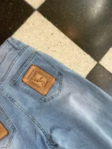 Jeans de mezclilla celeste de corte wide leg, con parches de cuero genuino bordados a mano en los bolsillos traseros.