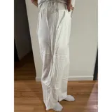 Pantalón palazzo de tiro alto, color blanco, con cierre frontal de doble botón y pinzas en la cintura. Presenta un corte wide leg y bolsillos laterales.