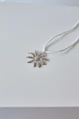 Collar con tiento trenzado color crema y dije de acero quirúrgico hipoalergénico con forma de sol o flor estilizada.