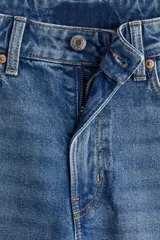 Pantalón de jean azul de corte ancho, tiro alto y largo tobillero. Cuenta con cinco bolsillos, cierre con cremallera y botón.