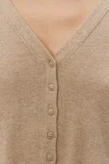 Cardigan de punto fino color beige, con escote en V, cierre frontal de botones y mangas largas.
