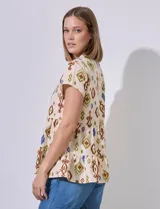 Blusa color crema con estampado tribal en tonos marrón, verde y azul. Tiene cuello a la base, escote en V, abertura central con botones, corte en la cintura con volados y ruedo con volados.