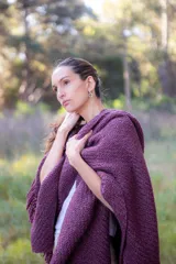 Ruana de lana merino extrafina con tejido texturizado, diseño envolvente y flecos en los extremos. Prenda versátil de corte amplio y sin género.