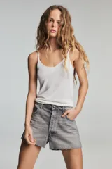 Shorts de denim gris claro con efecto lavado, tiro bajo y corte ancho (baggy). Presenta cinco bolsillos y cierre frontal con cremallera y botón metálico.
