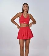 Conjunto deportivo compuesto por un top con escote en V y espalda deportiva, y una pollera short con diseño plisado. El top presenta el logo de la marca estampado en el frente.