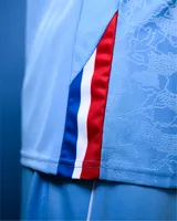 Camiseta de básquet Umbro de edición especial del Club Nacional de Football, color celeste con detalles en azul, blanco y rojo en el cuello y las sisas. Presenta el logo de Umbro y el escudo del club bordados en el pecho.