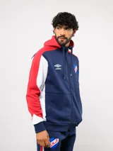 Campera deportiva Umbro del Club Nacional de Football, con cierre frontal, capucha ajustable con cordones y diseño en bloques de color azul, celeste y blanco. Presenta el logo de la marca y el escudo del club bordados en el pecho.