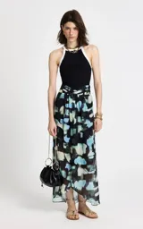 Pollera larga de corte evasé con estampado abstracto en tonos azules, negros y beige. Presenta cintura alta con diseño cruzado, pliegues suaves que aportan movimiento y un acabado con sutil transparencia en el bajo.