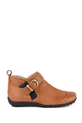 Botita baja Marcel de cuero vacuno color marrón, con interior de corderito sintético, costuras pespunteadas visibles, tira con hebilla metálica dorada y detalles elásticos laterales.
