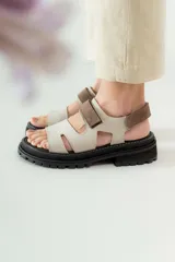 Sandalias de cuero marrón con diseño de tiras anchas y ajuste mediante velcro. Presentan una plantilla acolchada color tostado con detalles en rojo y una suela de goma negra con plataforma dentada.
