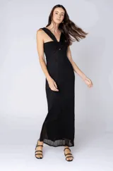 Vestido largo negro de tejido acanalado con hilos brillantes. Presenta escote asimétrico de un solo hombro con detalle anudado y abertura en el busto.