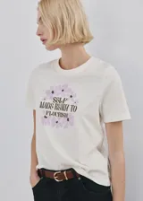 Remera de algodón color blanco, con cuello redondo y mangas cortas. Presenta un estampado frontal con flores en tonos lila y la frase "Self made ready to flourish" en letras negras.