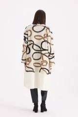 Spolverino largo de tejido de punto en color crudo, con diseño de patrones geométricos en tonos marrón y negro. Presenta un corte abierto con solapas amplias y mangas largas.