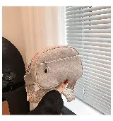 Cartera bandolera pequeña color beige, de cuero sintético con textura granulada. Tiene correa ancha de tela estampada con motivos geométricos y cierre superior con cremallera. Incluye un bolsillo frontal con cremallera y un dije metálico.