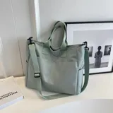 Bolso tipo tote color gris claro, con doble asa de mano y correa larga regulable. Tiene dos bolsillos laterales y un bolsillo frontal.