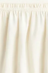 Minifalda holgada de viscosa color marfil con inserciones de encaje. Presenta cintura elástica con ribete de picot y frunces en todo el contorno, silueta ligeramente acampanada y dobladillo redondeado con abertura en cada lateral.