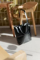 Cartera tipo tote bag de cuero marrón, con diseño minimalista, asas largas y detalles de remaches metálicos en la unión de las asas.