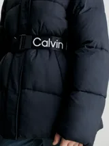 Campera puffer negra de nailon con capucha y cinturón con hebilla. Tiene cierre de cremallera y botón de presión, bolsillos en la cintura y logo monograma de Calvin Klein estampado en el pecho.