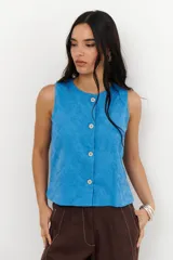 Top sin mangas color beige con cuello redondo y cierre frontal de botones. Presenta un delicado bordado floral en toda la prenda.