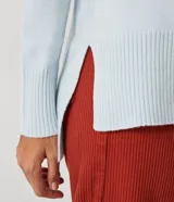 Suéter de tejido de punto color beige con cuello alto, mangas con corte raglán y puños y ruedo acanalados. Presenta un diseño clásico y cómodo con el ruedo trasero ligeramente más largo.