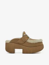 Zueco de plataforma alta confeccionado en cuero vacuno color tostado con forro de pelo de oveja. Presenta una correa con hebilla metálica ajustable en el empeine y suela de goma con diseño acanalado.