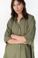 Camisa de manga larga color verde militar, con cuello camisero, cierre frontal con botones y diseño amplio.
