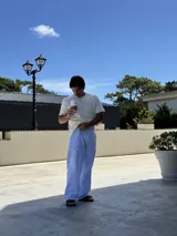 Pantalón de corte ancho y holgado, con diseño de rayas verticales finas en color azul y blanco. Presenta cintura elástica con cordón ajustable y un pequeño bordado en color rojo en la parte superior.