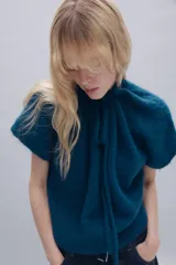 Jersey de punto de textura suave en color azul, con cuello redondo ajustable mediante cordones del mismo tejido y manga corta.