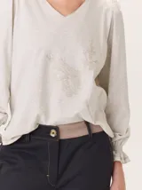Remera de algodón con cuello en V, mangas largas con puños elásticos y volados, y estampa botánica sutil en el frente.