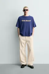 Remera de algodón con cuello redondo y manga corta, de corte holgado. Presenta un estampado frontal con la frase 'Sonic Bloom' en color amarillo.