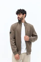 Campera de algodón con cierre frontal, cuello alto en color verde oliva y cuerpo texturado con patrón de espiga en tono marrón topo. Las mangas son lisas y del mismo tono que el cuerpo. Presenta un pequeño logo bordado en el pecho.