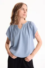 Blusa negra de manga corta, confeccionada en tela crepé, con detalle de fruncido en el escote redondo y pequeña abertura frontal en V.