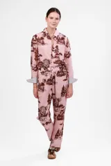 Pantalón largo de tela color rosa con estampado de leones y árboles en color marrón. Tiene cintura elástica y bolsillos laterales.