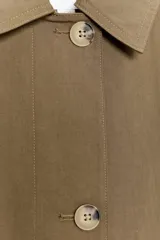 Chaqueta de corte recto y estilo camisero en color beige, con cuello solapa, manga larga y cierre frontal con botones. Presenta dos bolsillos delanteros de plastrón.