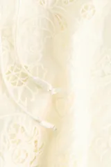 Blusa de lyocell color marfil con diseño de broderie tono sobre tono, cuello redondo fruncido, escote en V con cordón para atar y mangas largas raglán con ribetes festoneados.