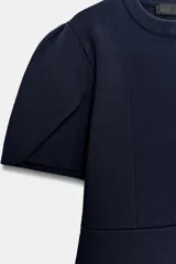 Chaqueta entallada azul marino de punto, con cuello redondo y mangas cortas abullonadas con aberturas. Cierre frontal con botones forrados a tono.