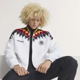 Campera deportiva Adidas de la selección de Alemania, inspirada en el diseño de 1994. Es de color blanco con un estampado geométrico en los hombros que combina los colores de la bandera alemana (negro, rojo y amarillo). Presenta cierre frontal, cuello redondo y el logo de la marca junto al escudo de la DFB en el pecho.