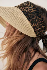 Visor de ala ancha tejido en paja natural, con banda frontal y lazo trasero en tela con estampado de leopardo.