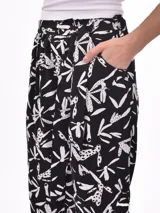 Pantalón babucha de tiro alto con cintura fruncida y lazo para ajustar. Estampado de hojas tropicales en tonos naranja y marrón sobre fondo blanco.