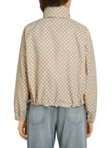 Campera deportiva Tommy Hilfiger color beige con estampado de logos en marrón. Tiene cuello alto, cierre de cremallera, dos bolsillos laterales con botones, puños elásticos y logo bordado en el puño.