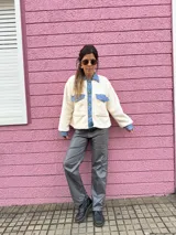 Chaqueta color crema de corderito con detalles en jean azul en cuello, solapa, bolsillos y puños.