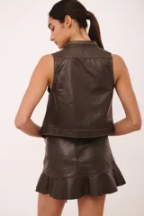 Top sin mangas de cuero color marrón oscuro, con cuello tipo camisa y cierre frontal anudado con tiras de cuero. Presenta pespuntes contrastantes en color claro.