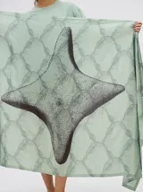 Pareo largo de viscosa en color verde menta, con diseño estampado que presenta gráficos abstractos y una figura central destacada en negro. Es una prenda liviana y fresca, ideal para usar sobre el traje de baño o como falda envolvente.