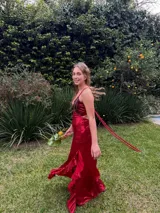 Vestido largo rojo satinado, con escote en V, tirantes finos cruzados en la espalda, aberturas laterales (cut out) en la cintura y falda larga con tajo y volados.