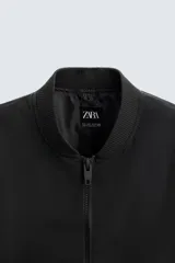 Cazadora bomber ligera de tejido técnico color verde oliva, con cuello, puños y bajo en rib elástico. Presenta cierre frontal de cremallera y bolsillos de vivo en la cadera.