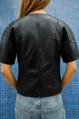 Cuerpo crop efecto piel de color negro, con cuello redondo y manga corta. Presenta costuras marcadas y cierre frontal con cremallera metálica.