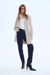 Saco largo de punto fino color beige, con lana en la trama, hombros caídos y ribete acanalado en nuca, puños y bajo. No tiene cierre.